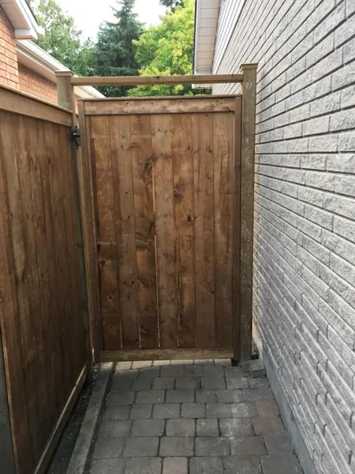 Tall wood gate installed in a narrow passage between two houses, on paving stones