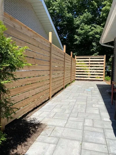 Horizontal slat wood fence with matching gate, along a paving stone walkway