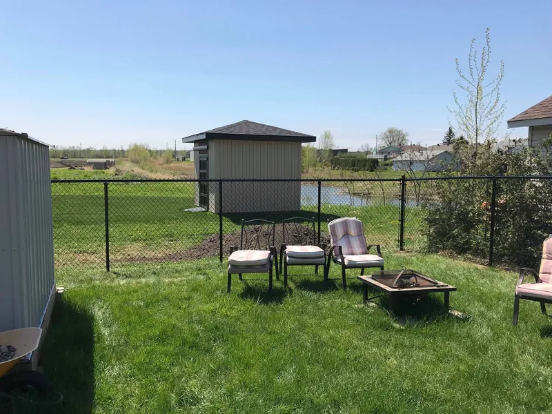 Black chain link fence at the rear of a yard, open field beyond