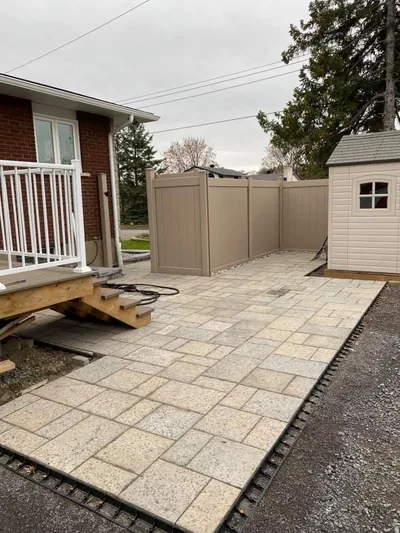 Beige PVC fence along a paving stone patio, garden shed behind