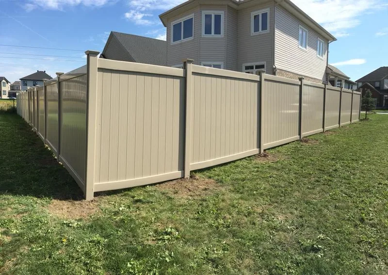 Beige PVC fence following the slope of a yard